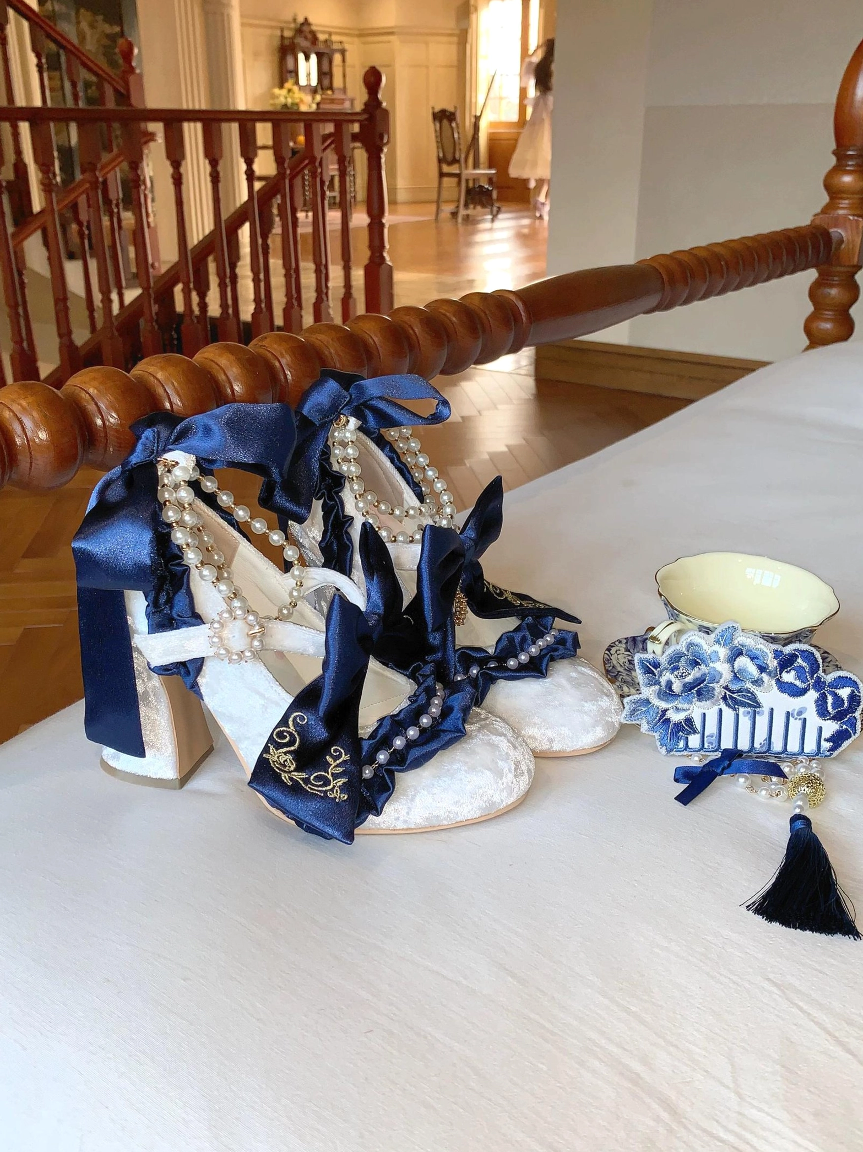 Navy blue oversized satin bow lolita heels with pearl decorations embroidered fabric and matching pearl tassel hair clip on wooden desk