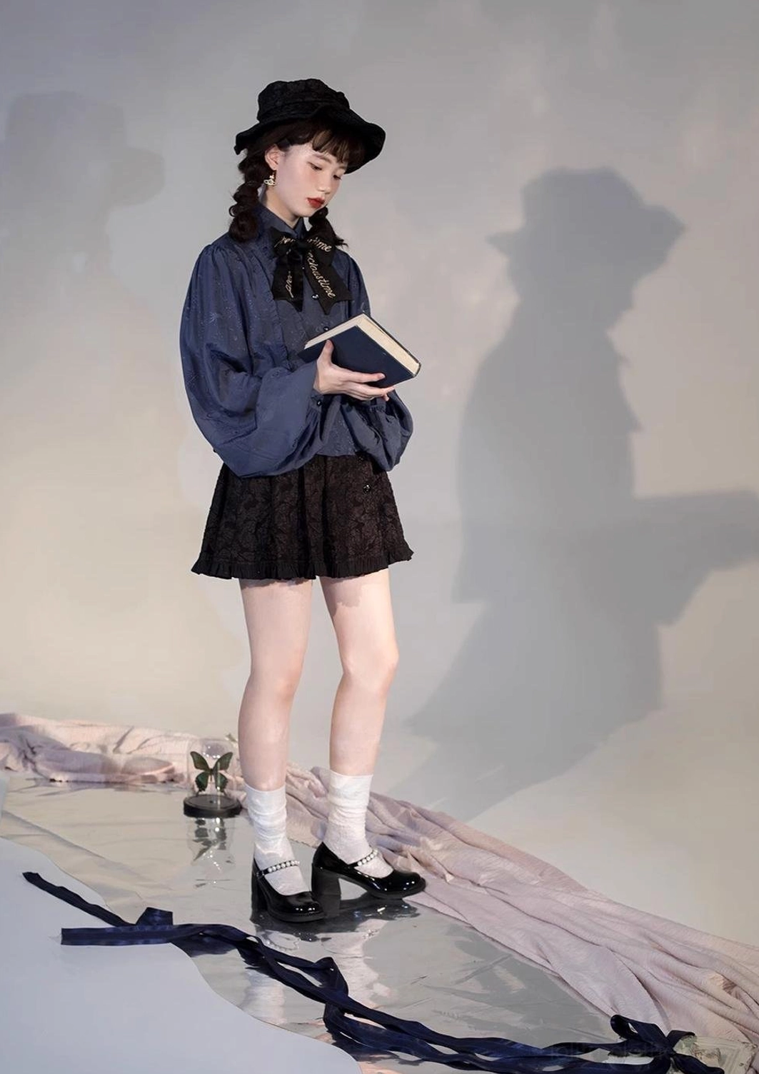 Navy blue retro Lolita blouse styled full body outfit studio shot model wearing black mini skirt bow tie fedora hat with minimalist shadow studio background