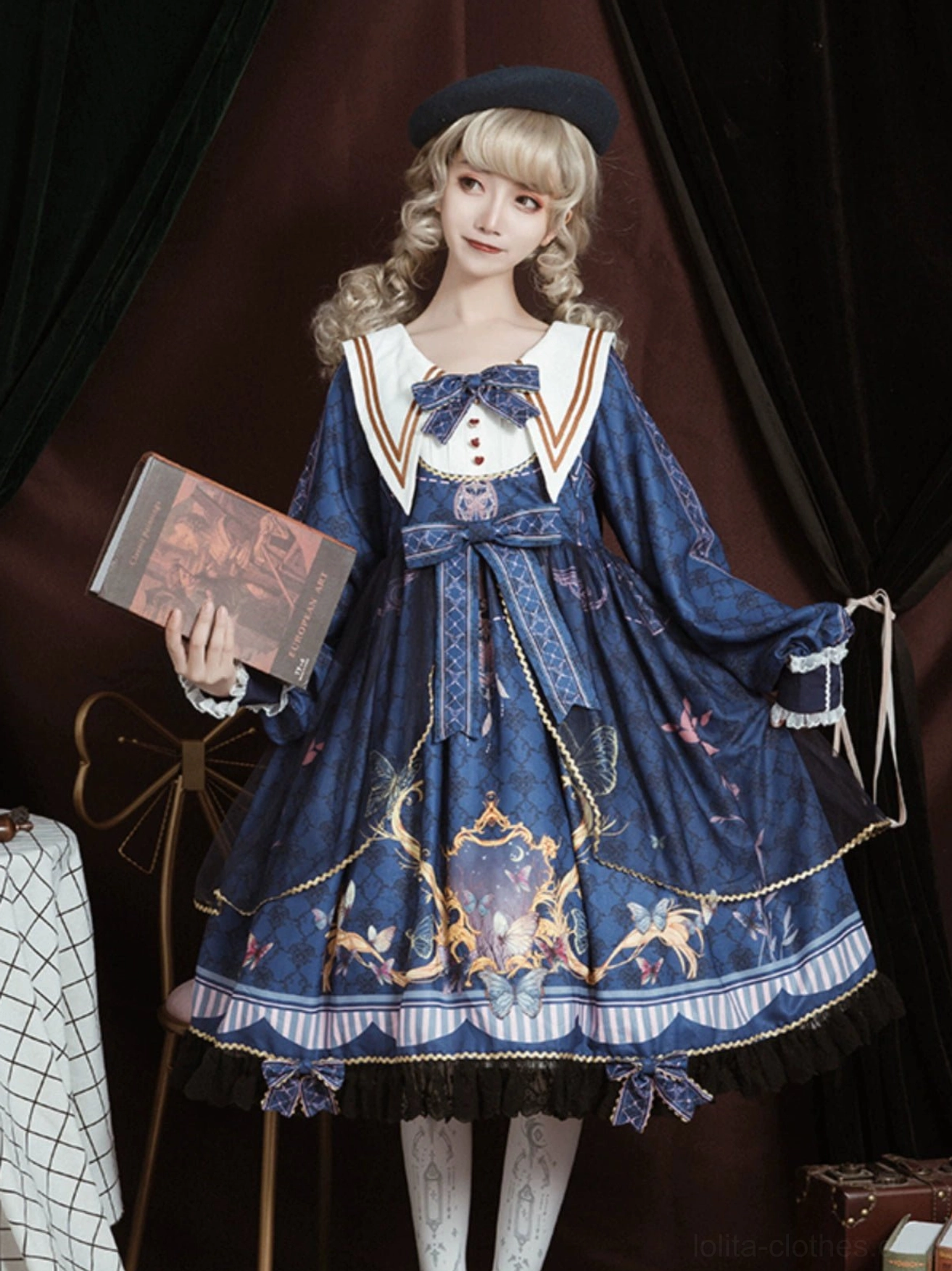 Classic navy blue sailor collar lolita one-piece dress front view on model with blonde curly hair, white sailor collar with gold trim, front blue bow, large waist bow, royal baroque print skirt with striped ruffled hem and black lace trim