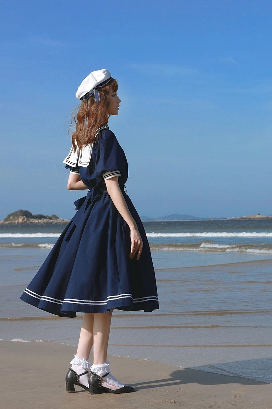 Navy blue sailor lolita OP dress full body side profile female model wearing matching sailor hat wet beach maritime aesthetic