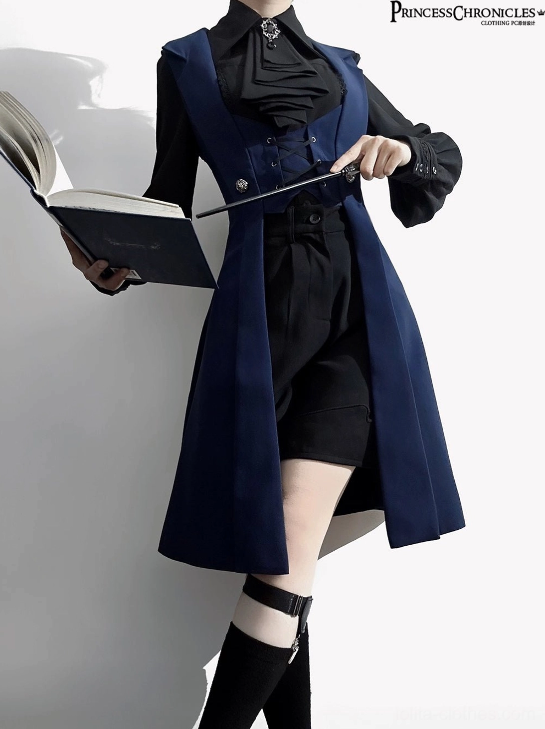 Night Prelude Gothic Ouji Lolita vest front three-quarter fantasy styling shot with prop accessories, model holding decorative book and wand, single thigh strap on left leg, signature ruffled ascot with brooch