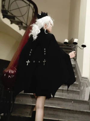 Back view of gothic ouji lolita complete set showing bat-wing cape hem, silver cross embellishments, model with candelabra prop in vintage staircase setting