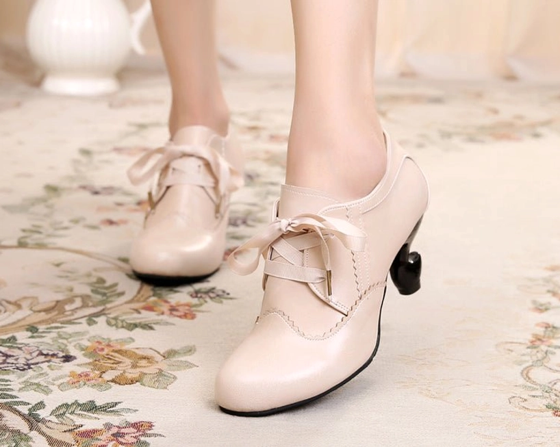 Nude beige light retro lace-up Lolita high heel shoes with delicate scalloped stitching, curved spool heel, and ribbon lace fastenings, styled on indoor floral area rug