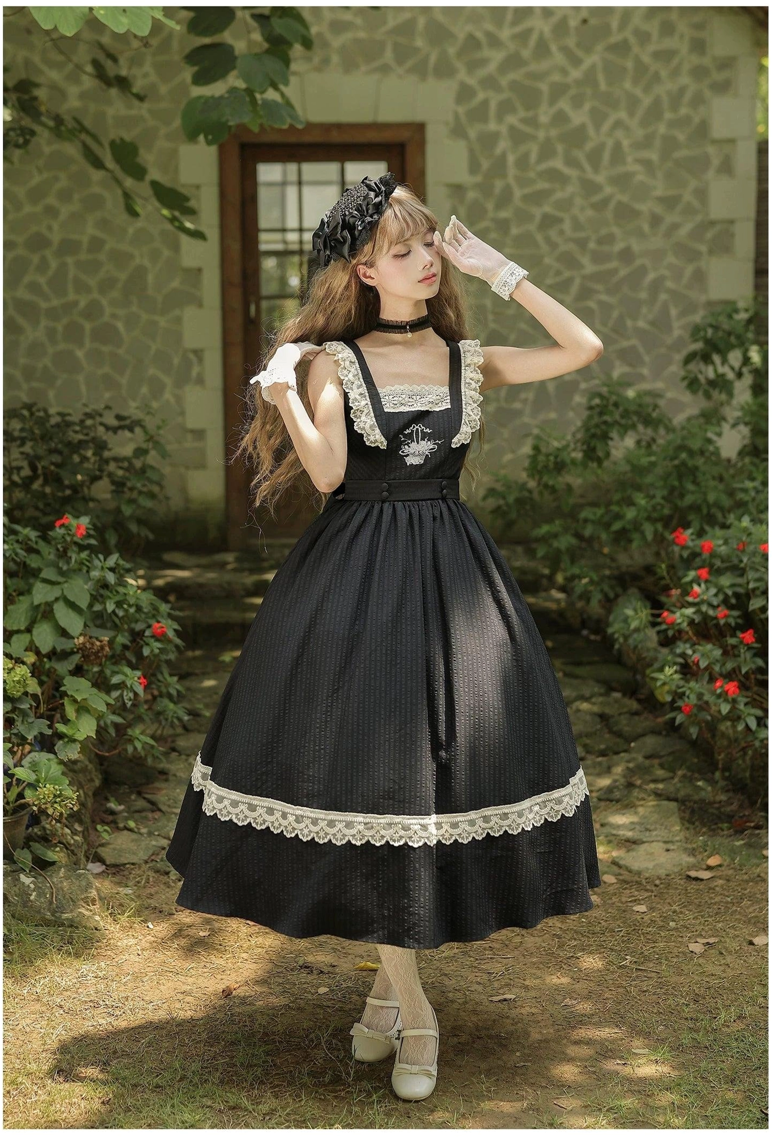 Black classic lolita JSK dress with square lace neckline and rose basket bust embroidery detail, slim high-waisted silhouette shown in front view outdoor stone house courtyard