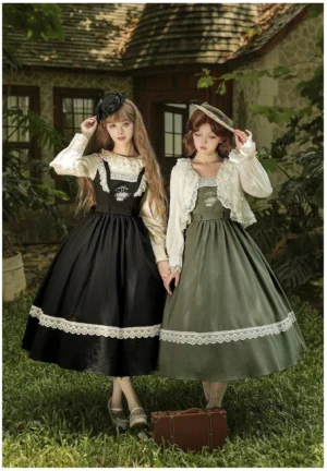 Two models wearing vintage lolita coordinate sets in sage green and black with rose basket embroidery, standing together in front of rural courtyard with vintage suitcase, showing classic JSK dress options