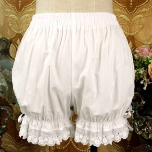 Off-white cotton Lolita bloomers with embroidered scalloped lace ruffles and satin ribbon bows on leg cuffs, displayed on dress form with vintage European floral backdrop, showing gathered puff silhouette and leg hem details
