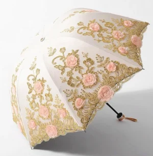 Off-white foldable lolita parasol with gold thread embroidery and three-dimensional pink rose patterns, featuring scalloped lace edge and metal handle with hanging strap, displayed fully open from top three-quarter view against studio white background