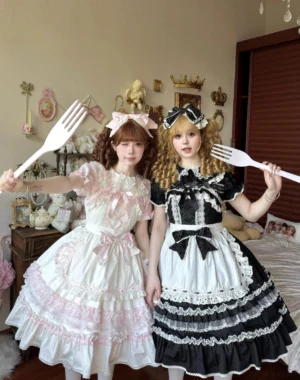 Two cream-colored Old School Lolita JSK dresses displayed on models in vintage bedroom setting with decorative fork props, showcasing layered ruffled skirts and lace trim details