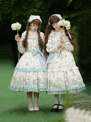 Oriole Time Country Lolita dress worn by two models in cream and blue color scheme standing on garden lawn with white floral props, showing front full-body view of JSK and OP styling options