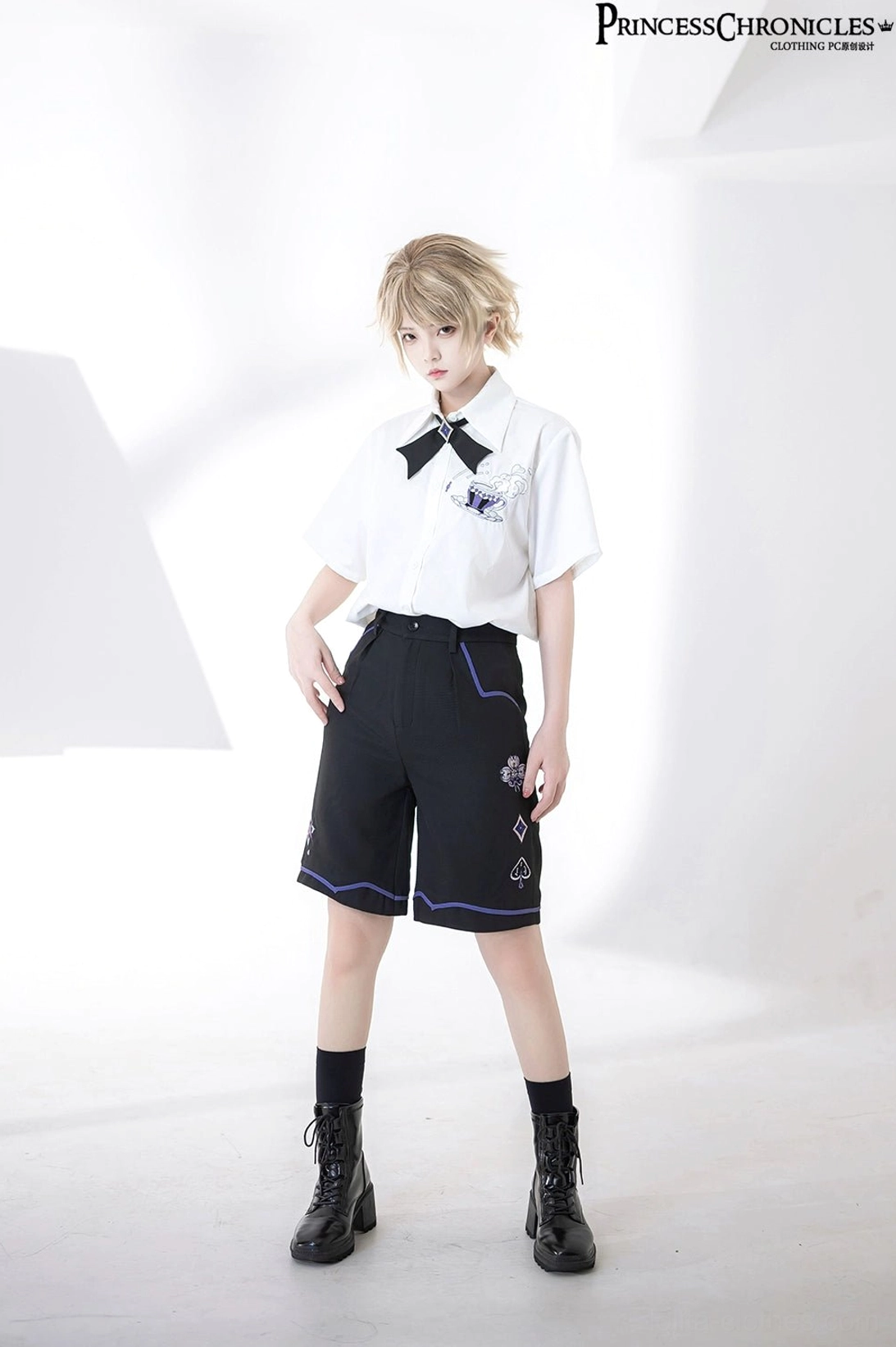 Half-body front view of androgynous model wearing ouji embroidered short-sleeve shirt with exquisite chest details and black trim shorts