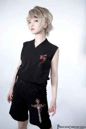 Blonde model wearing black ouji lolita sleeveless vest with red dragon chest embroidery and matching embroidered shorts, three-quarter front view in studio