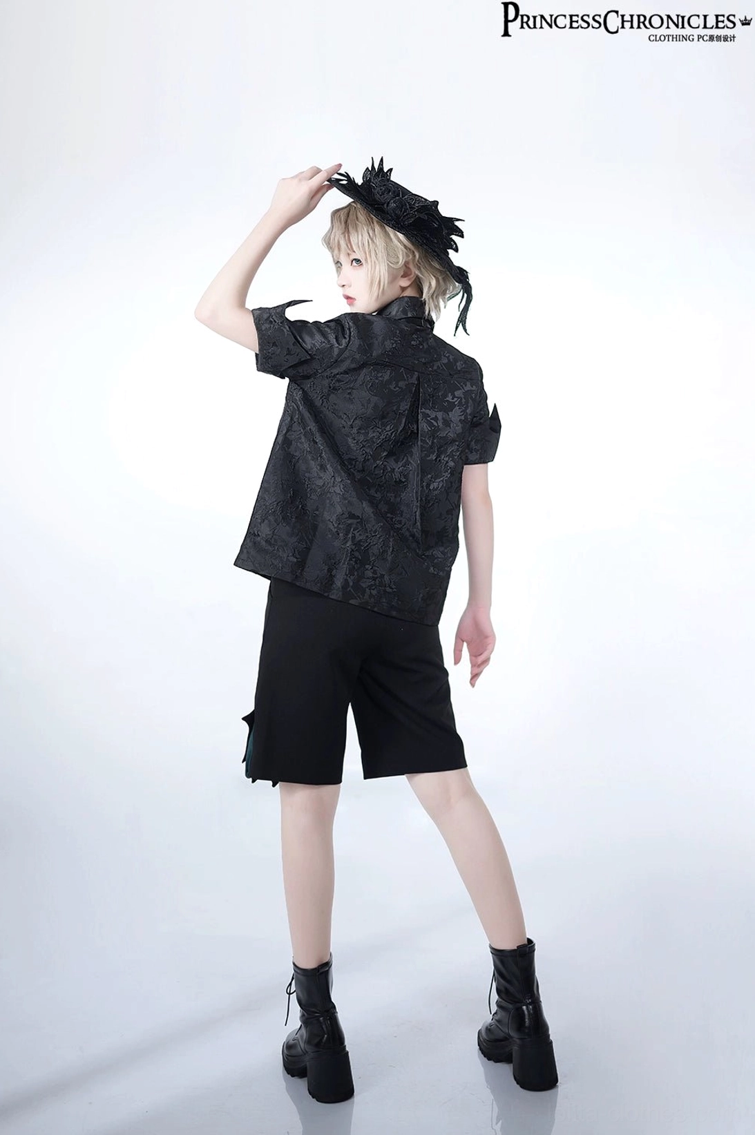 Ouji Lolita black hat gothic outfit full body rear three-quarter standing pose model hand near headdress jacquard shirt fit
