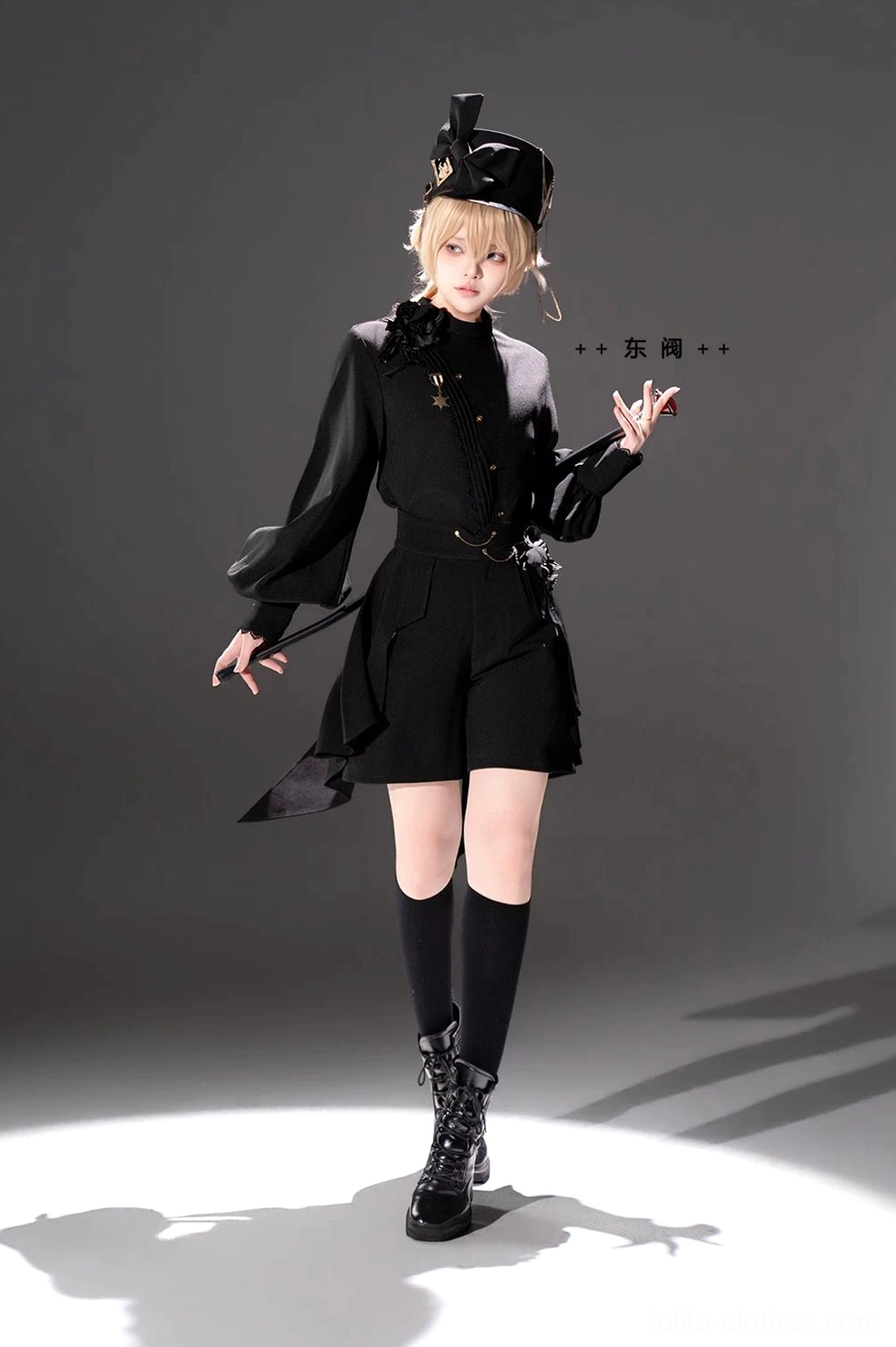 Black Ouji Lolita two-piece outfit front full body standing view with blonde model military hat hand behind back posing asymmetric back hem shorts