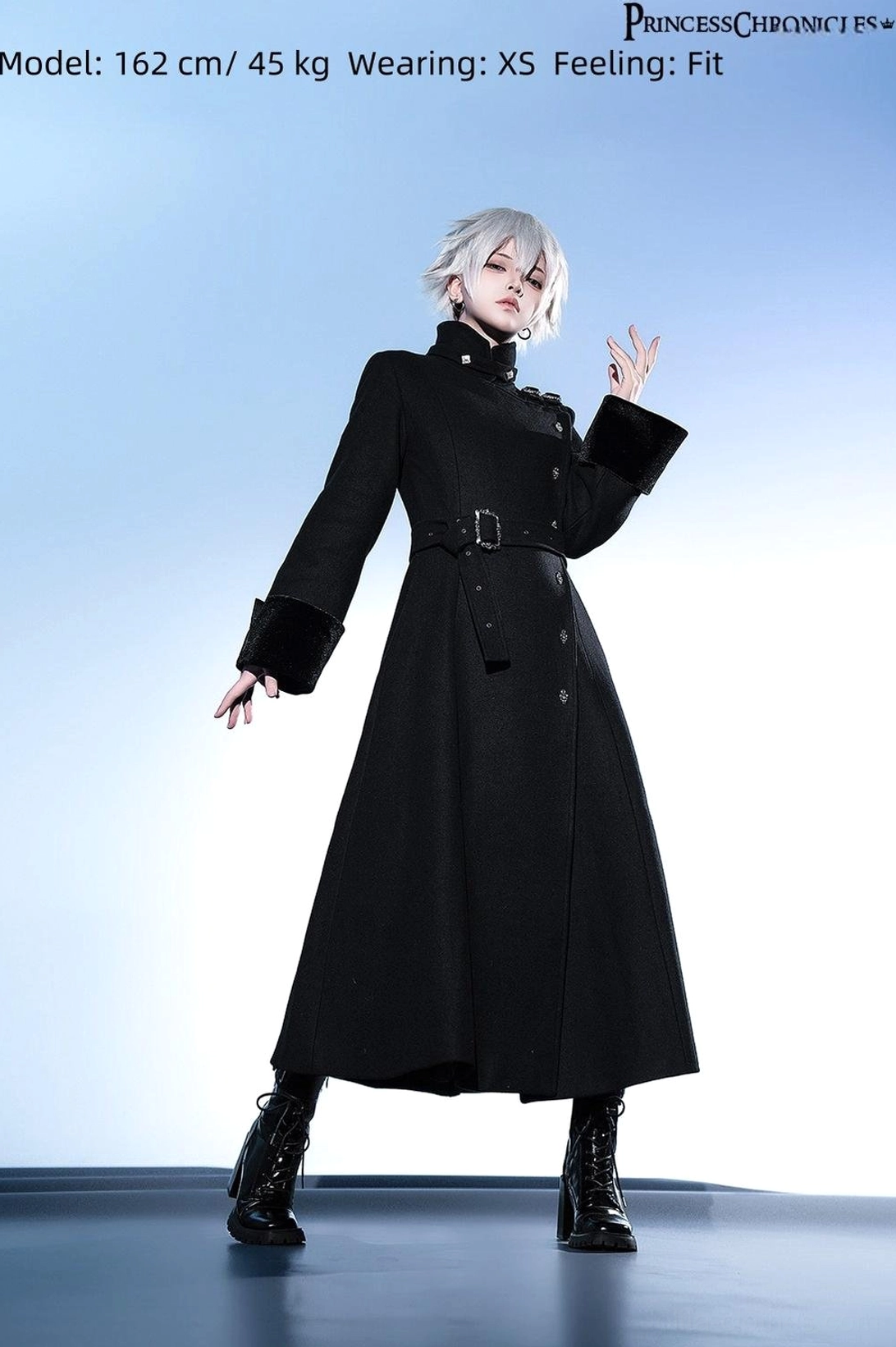 Side view of model in black Ouji Lolita overcoat wearing XS size showing flared long skirt hem elegant silhouette belted waist with combat boots on blue studio background