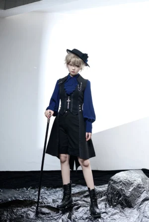 Full body frontal view of black and blue retro ouji lolita gentleman outfit with royal blue mutton sleeve shirt, black waistcoat with cross brooch, on androgynous model in studio setting with dark wet fabric and rock props