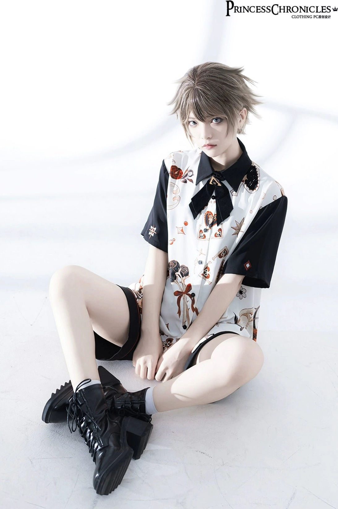 Ouji Lolita seated close-up front view showing detailed floral prints on shirt front, black combat boots with socks, upper garment embellishment details in studio setting