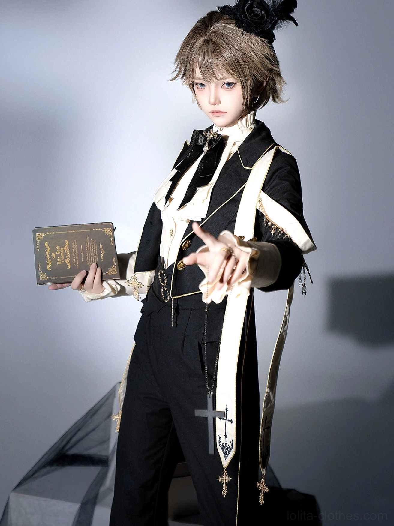 Gothic ouji lolita tailored suit close-up front view holding prayer book black feather hair accessory cross sash