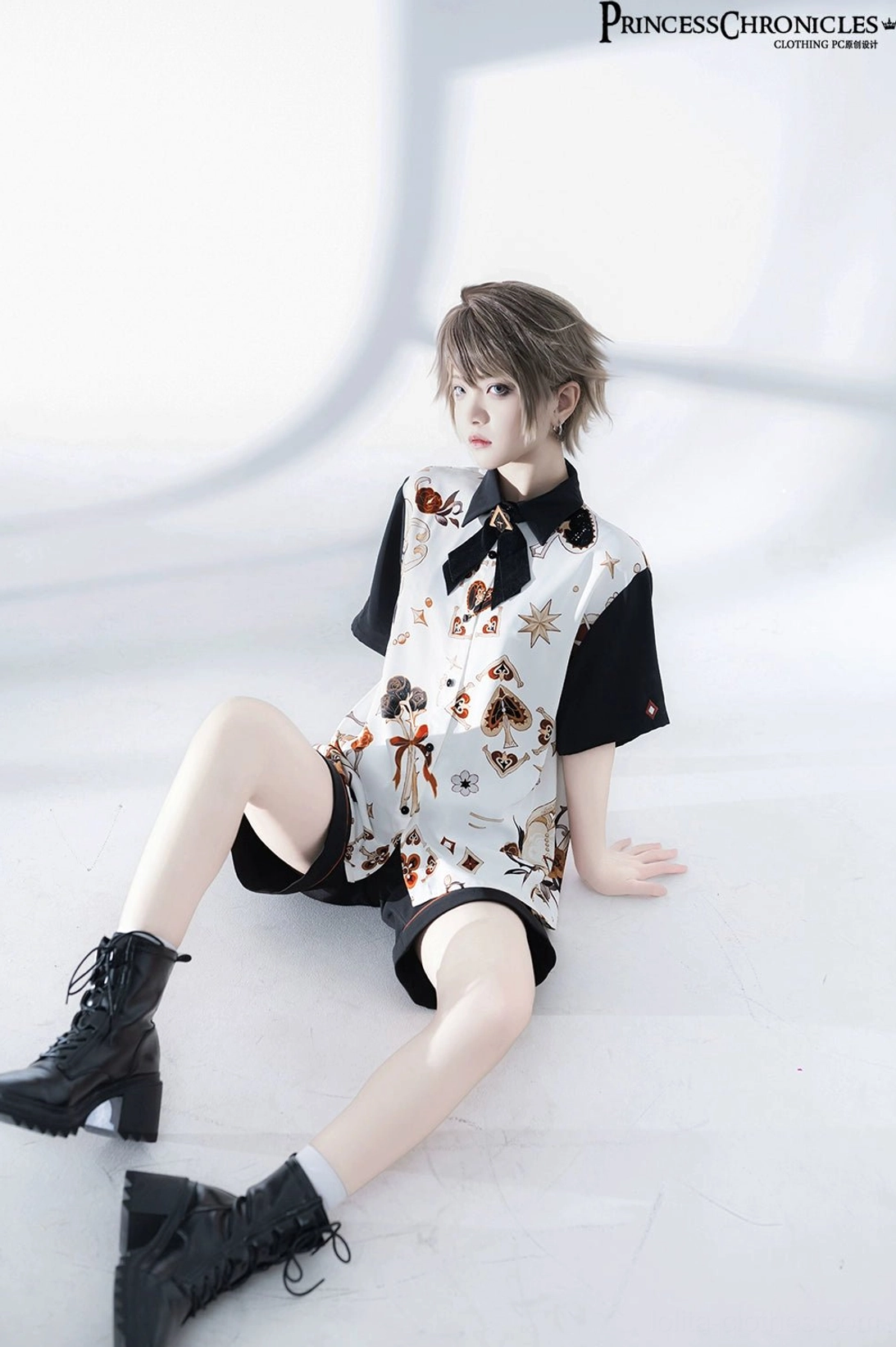 Low-angle seated pose view of retro Ouji Lolita suit displaying shirt hem, shorts construction, black boots styling, and overall ensemble proportions from floor perspective