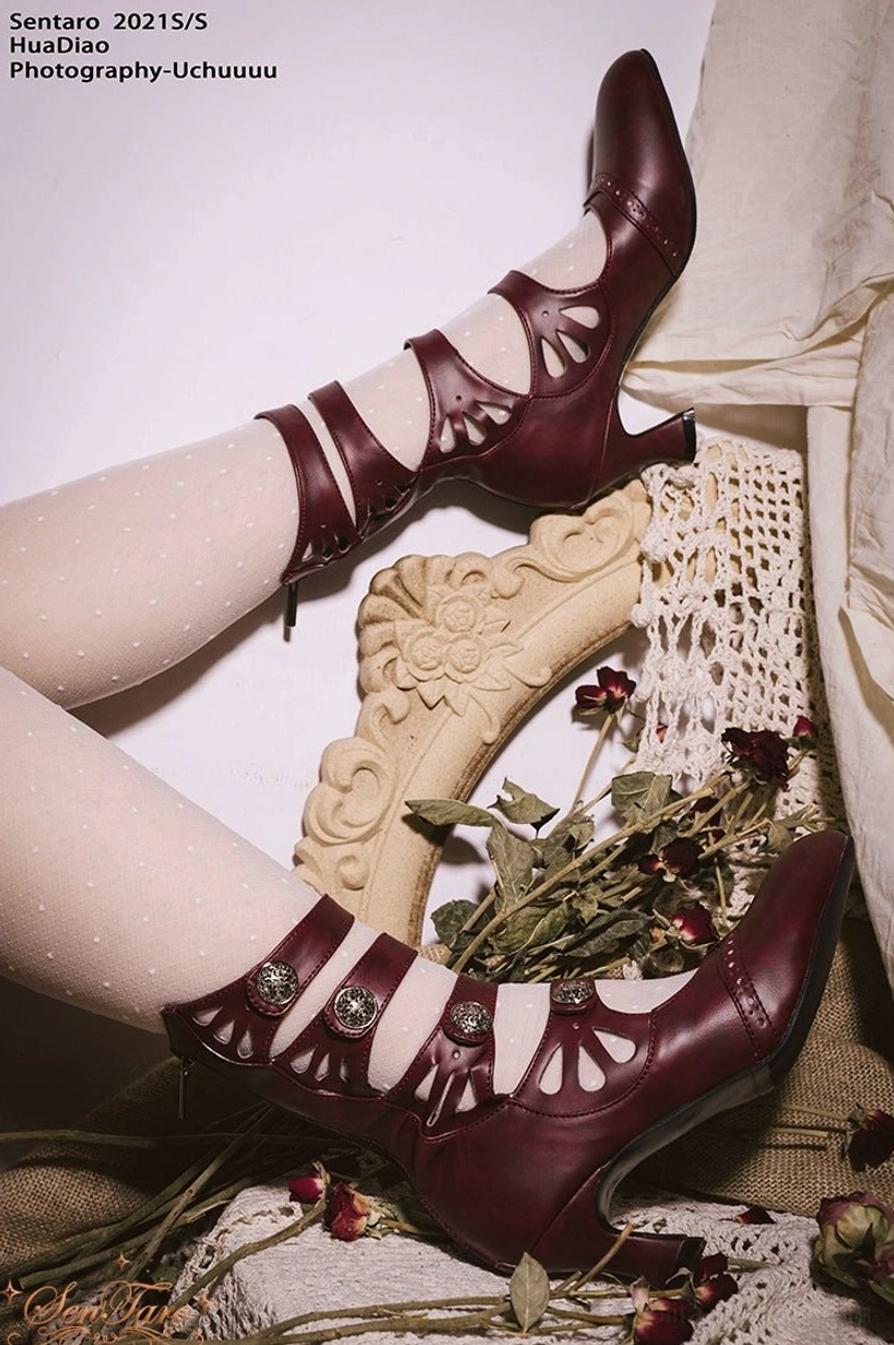 Pair of burgundy floral hollow-out Mary Jane Lolita ankle boots on white polka dot socks showing curved heel metal buckles and carved straps
