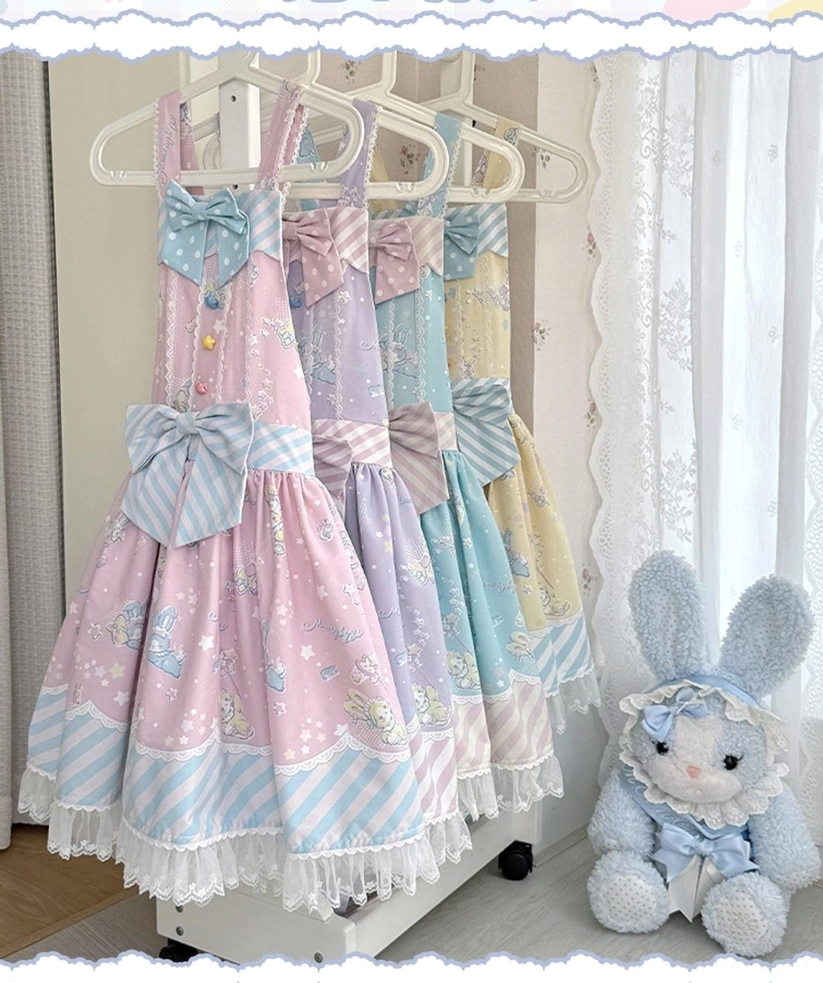 Flat hanging display of pastel-colored Lolita jumper skirt with large front bow, striped hem lace ruffles, and full skirt bottom, positioned on clothing rack with sheer curtain background and plush rabbit toy