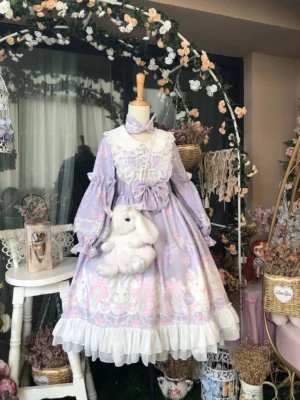 Pastel purple rabbit print Lolita OP dress front view on mannequin display with white doll collar, prominent front bow, floral arch backdrop, and coordinating rabbit plush bag accessory