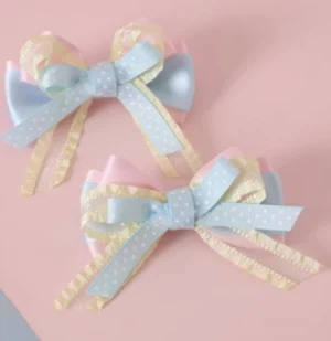 Pastel ribbon bow hair clips with blue pink and yellow layered satin dotted design and flowing ribbon tails flat lay view