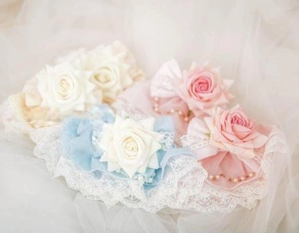 Flat lay close-up view of pastel rose Lolita hair clip set with mixed pink, sky blue and cream artificial roses, lace ruffled base with pearl beads displayed on sheer tulle fabric