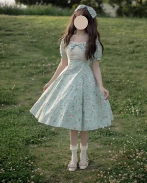 Model wearing light blue floral lolita op dress outdoors on grass lawn showing complete classic lolita coordinate with matching hair bow frilled socks leather loafers and square neckline bow detail