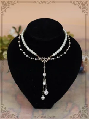 Double-strand pearl necklace with rhinestone-studded gold bow pendant and tassel, displayed on black velvet mannequin with vintage framing and floral accents - classic lolita jewelry