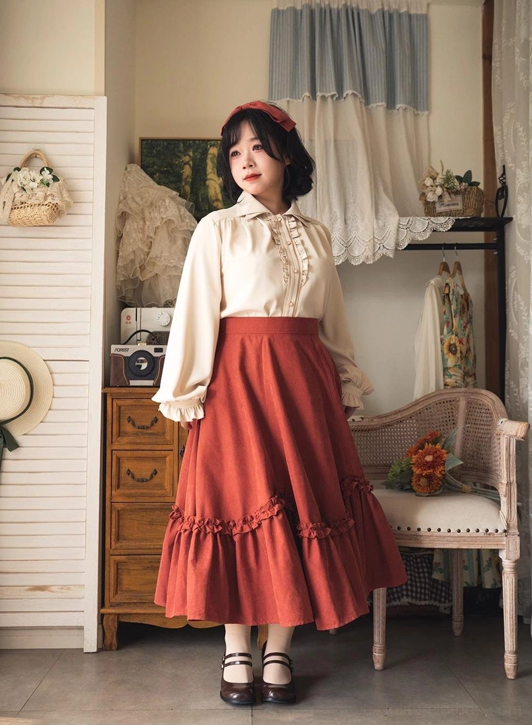 Model wearing full vintage Lolita coordinate with petal swing orange-red ruffled skirt, ivory blouse, and matching red hairband with classic Mary Jane shoes, retro boutique studio