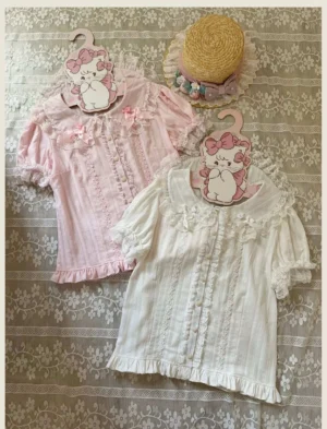 Classic Peter Pan collar short-sleeve lolita blouses in pink and off-white colors displayed flat lay with vintage lace fabric backdrop and decorative cat hangers