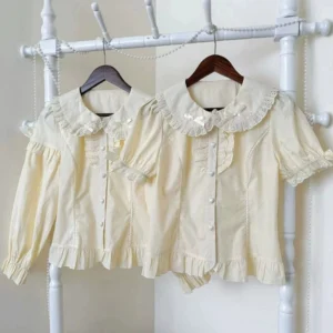 Short-sleeve Peter Pan collar lolita blouse with puff sleeves in white and apricot, displaying lace-trimmed doll collar and decorative shoulder bows on elegant white coat rack display