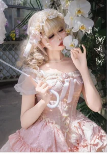 Pink ballet-inspired sweet lolita mini JSK dress with off-shoulder sheer puff sleeves, pearl necklace, satin bow bodice details, and flower headdress - close-up front model with parasol