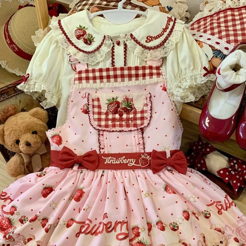 Pink-beige colorway lolita salopette dress flat lay display with matching red mary jane shoes, plush toys, gingham chest detail, strawberry embroidery, bow waistband with text