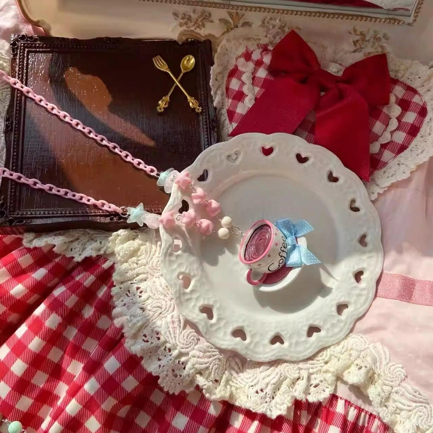 Pink-blue Lolita necklace featuring mini coffee cup pendant with blue polka dot bow and pink bead cluster chain displayed on white heart-shaped plate with red gingham cloth