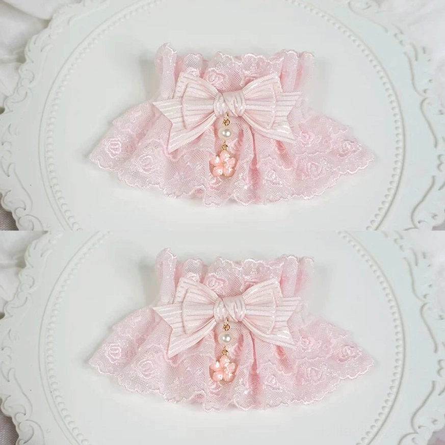 pair of pink lolita lace wrist cuffs with polka dot satin bow and rose embroidery flat lay on vintage white tray with linen background