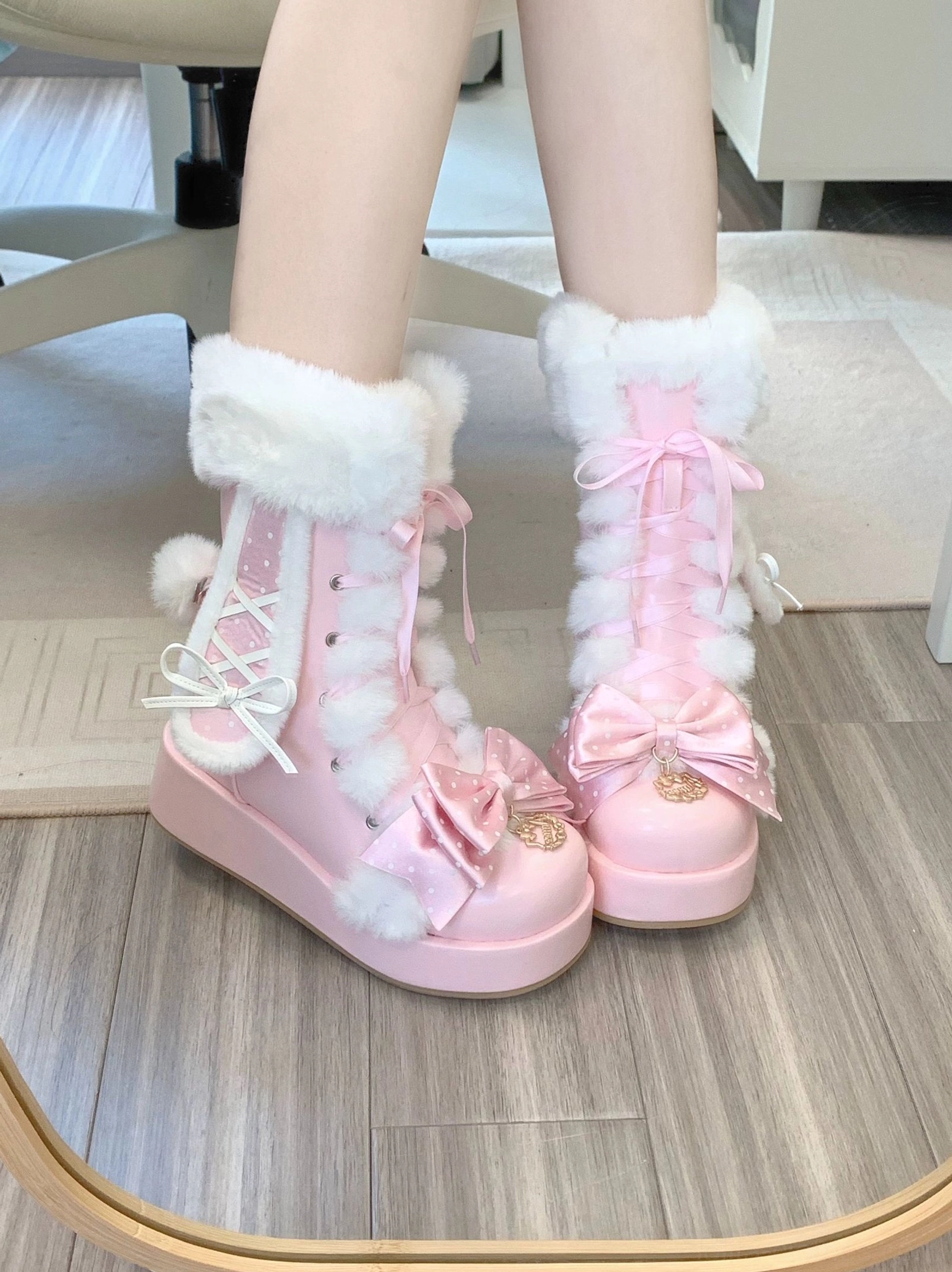 Mirror reflection of pink sweet lolita bunny ear platform boots worn on model's legs indoors, featuring white fluffy fur collar, front lace-up design, pink bow ornaments, and thick platform sole