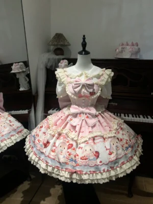 Pink sweet lolita JSK dress front view featuring bunny cake strawberry allover print, ruffled off-shoulder neckline, large front bow, and multi-layer lace hem trim displayed on dress form