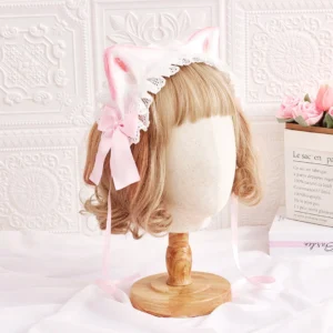 Pink cat ears Kawaii Lolita headband with white ruffled lace trim and pink satin bow on blonde mannequin displayed against embossed white wall