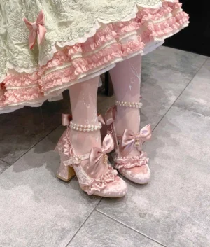 Pink Classic Lolita block heel shoes with pearl ankle strap and detachable satin bow, front low-angle view worn with ruffled pink-green Lolita skirt and butterfly patterned stockings