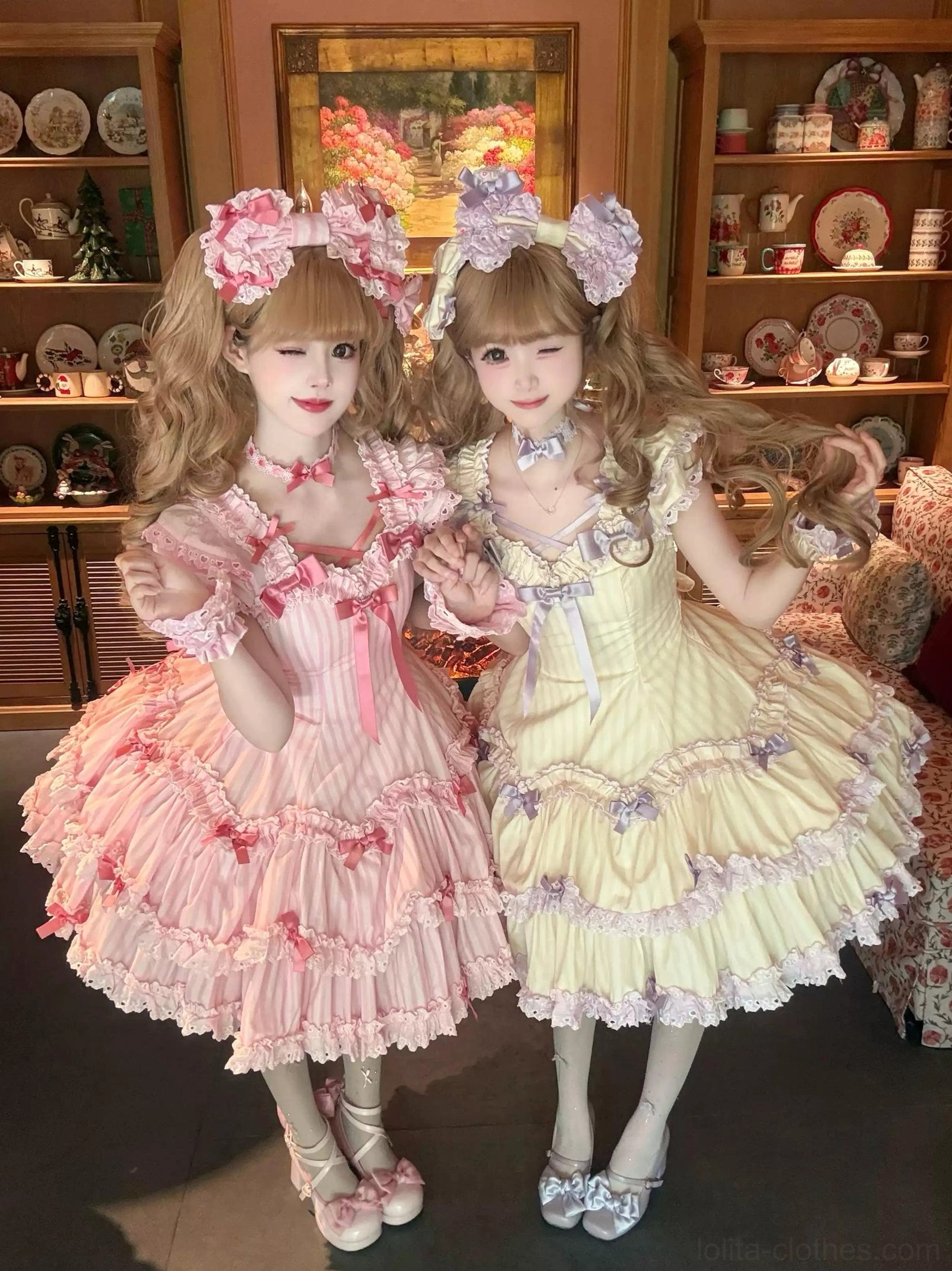 Two vintage colorways pink and cream yellow striped Lolita JSK dresses on models with flower hair crowns and vintage leather Mary Jane shoes indoors