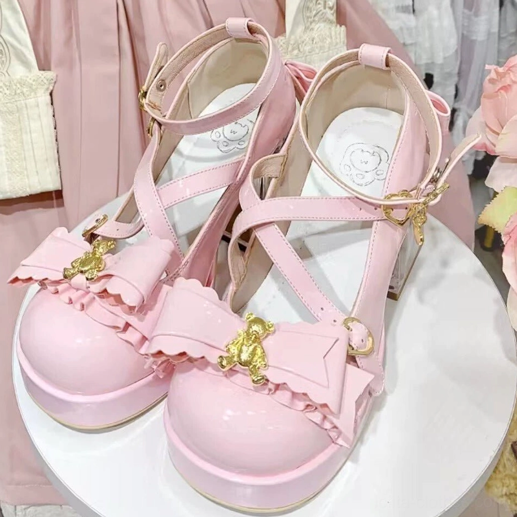 Pink dreamy bear sweet lolita platform heels on white display stand, front close-up shot, pink lolita dress fabric backdrop, patent leather finish, crisscross ankle straps, ruffled bow with gold bear charm, clear block heel