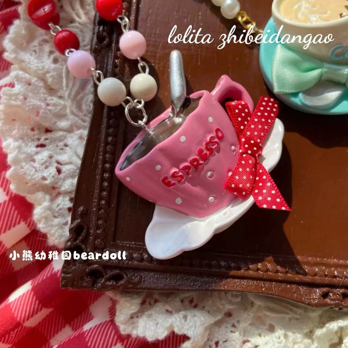 Pink espresso cup Lolita necklace with espresso text and red polka dot bow paired with colorful mixed bead chain in close-up shot on dark wooden tray
