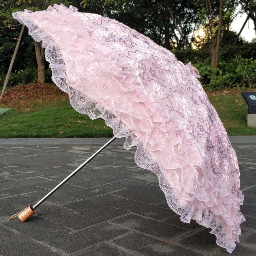 Pink floral lace Lolita parasol with multi-layer ruffled skirt featuring delicate embroidery and classic wooden handle, outdoor garden courtyard background
