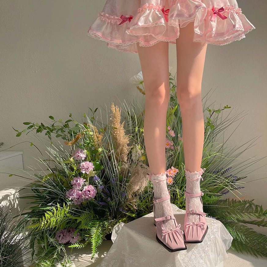 Pink delicate floral lace ankle socks with ruffled cuff and pink square-toe Lolita Mary Jane shoes displayed on model wearing pink frilly skirt with greenery backdrop