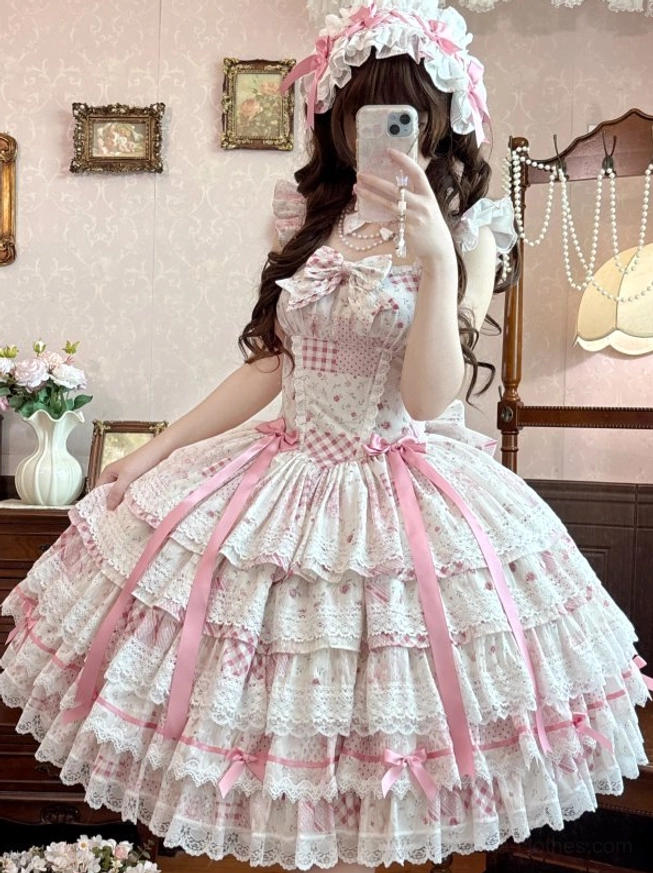 Back view selfie of pink floral lolita jumper skirt dress showing halter neck straps, large gingham back bow, and layered lace ruffles on model with brown curly hair