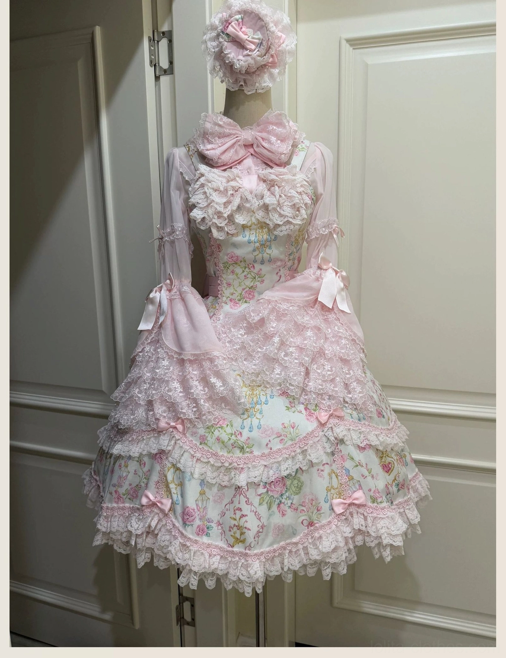 Pink floral Lolita JSK dress form display showing ruffled lace neckline, oversized front satin bow, layered lace skirt and pastel floral print