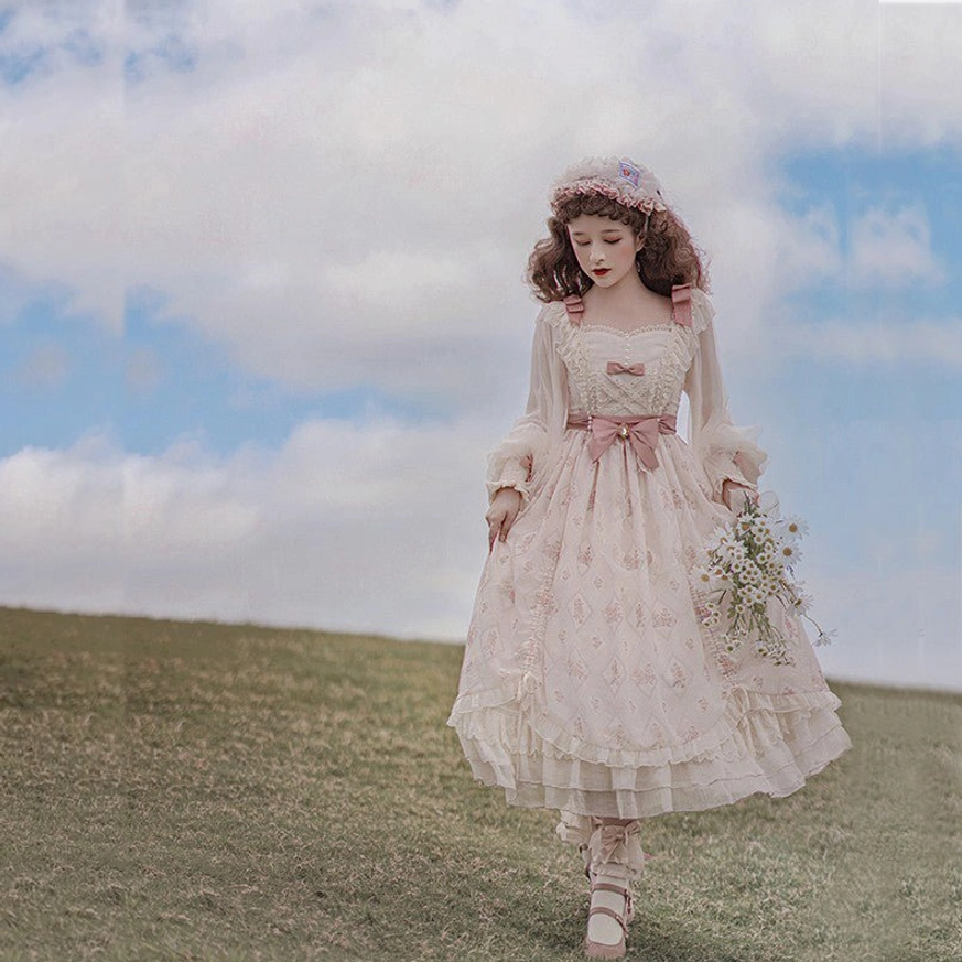 Full pink floral print lolita OP dress front view with small front neck bow, tiered ruffled skirt, model holding flower bouquet in open grassland setting, classic princess lolita aesthetic