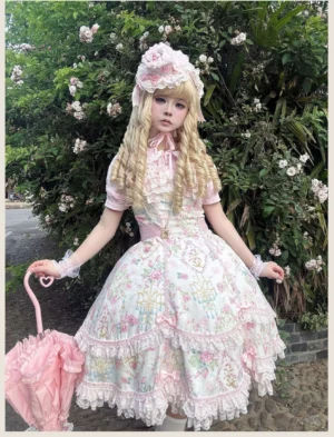 Pink floral old school Lolita JSK dress with lace trims and petal hem, modeled with matching bonnet and curly blonde hair in outdoor garden setting