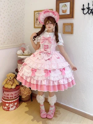 Front full-body view of pink fondant dream sweet lolita jsk dress with tiered ruffles, large front bows, and matching pink bonnet, paired with pink frilled socks and pink Mary Jane shoes in vintage dessert-themed studio
